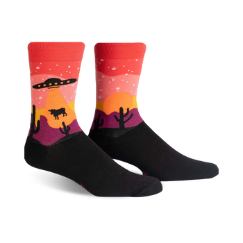 area 51 themed novelty socks feature a desert scene with a cow, cacti, flying saucer, and mountain.   