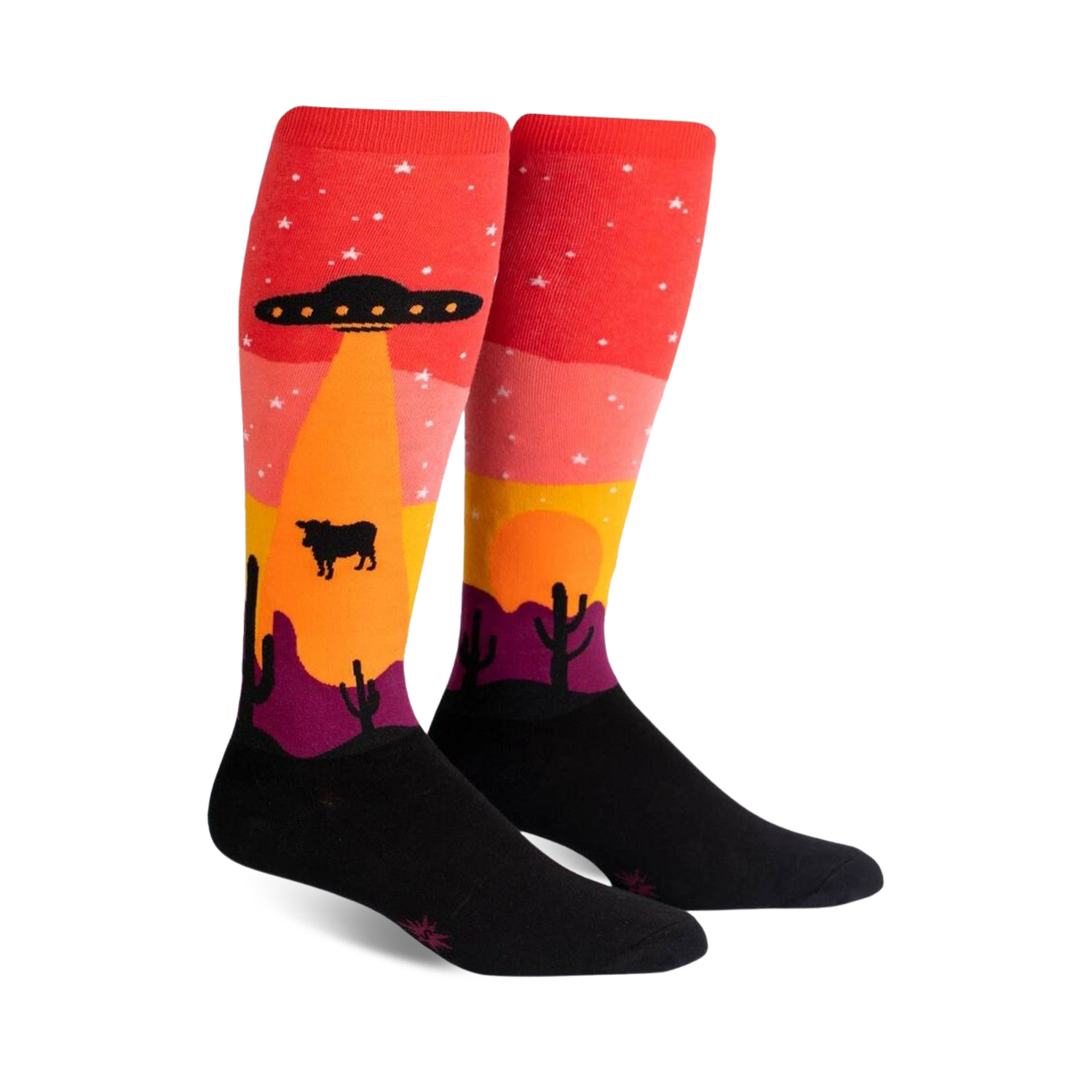 Pair of knee-high socks; red, orange, yellow, purple, and black. Design features an alien spaceship abducting a cow in a desert landscape at sunset.