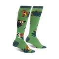 A pair of green knee-high socks with illustrated lemurs, fossa, and tropical leaves. Brown, white, and dark-green details on a bright green background.