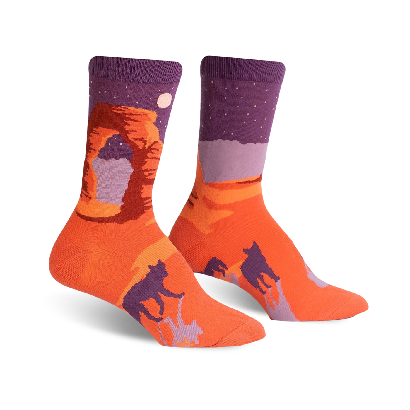 A pair of crew socks showcasing Delicate Arch National Park.  The socks are predominantly orange and purple, featuring the arch, a night sky, and dark silhouettes of bobcats.