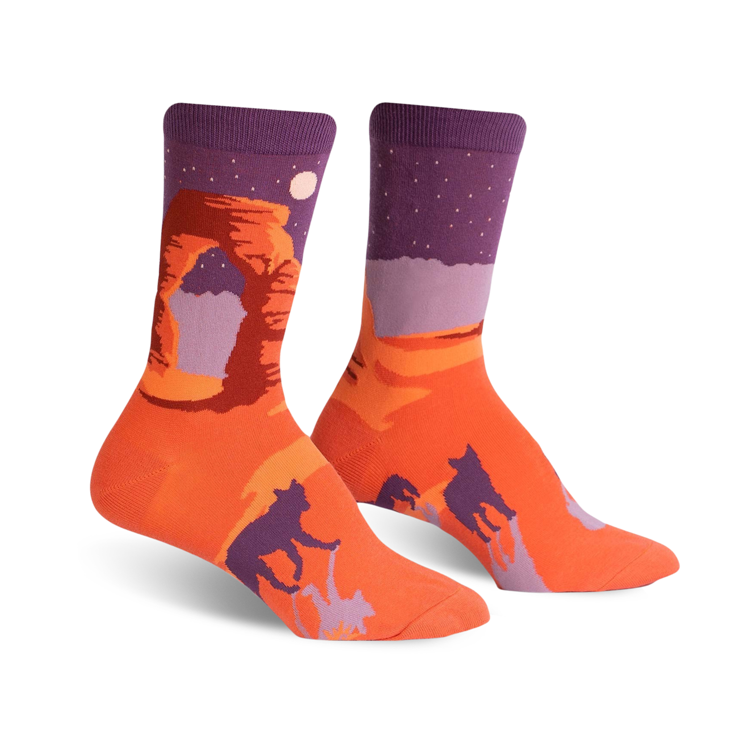 A pair of crew socks showcasing Delicate Arch National Park.  The socks are predominantly orange and purple, featuring the arch, a night sky, and dark silhouettes of bobcats.