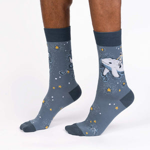 A pair of gray socks with an astronaut riding a narwhal in space on them. The astronaut is wearing a white spacesuit with a blue and red striped helmet. The narwhal is white with a blue horn. The socks are also covered in stars.