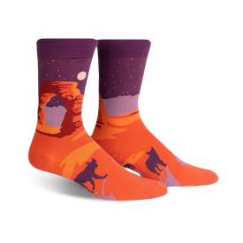 orange crew socks with purple cuff feature a desert scene with a large red rock formation, a moon, and two howling coyotes.   