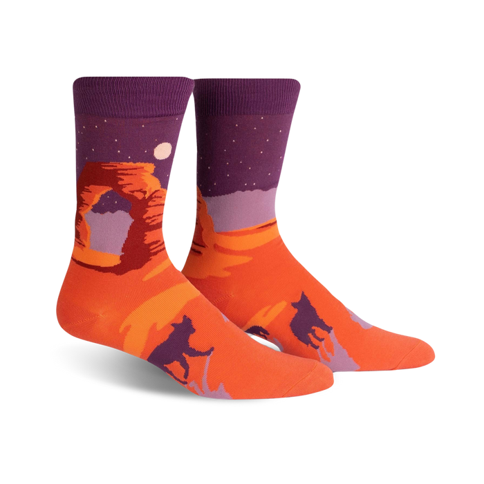 orange crew socks with purple cuff feature a desert scene with a large red rock formation, a moon, and two howling coyotes.    }}