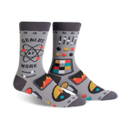 Pair of gray crew socks with a robot control panel design, atom graphic, and the phrase 'Genius at Work'. Features pops of orange, teal, and yellow.