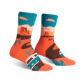 A pair of crew socks with a Monument Valley theme.  The socks are coral orange with a brown winding road, teal camper van, and cacti against a teal sky.