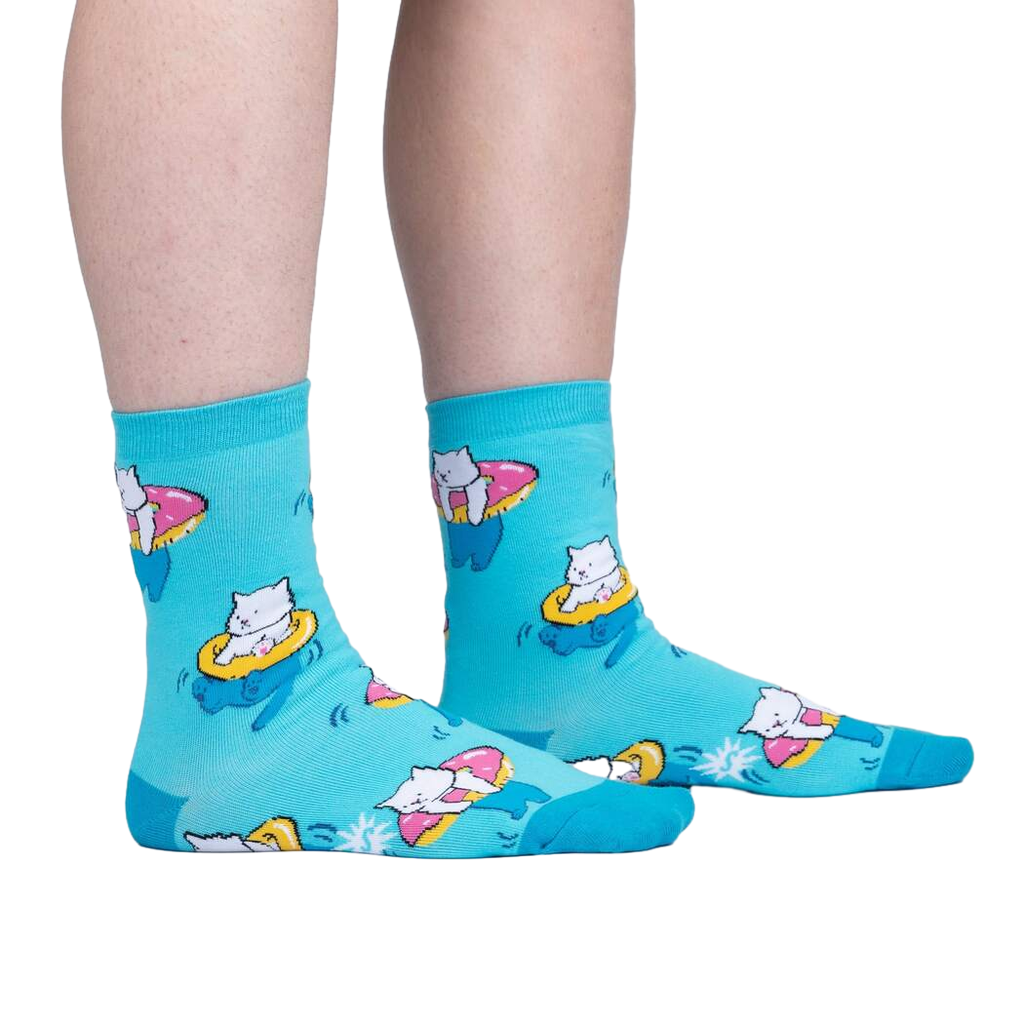 Lifestyle shot showing the socks on a person's feet; teal crew socks with white cats on donut floats.
