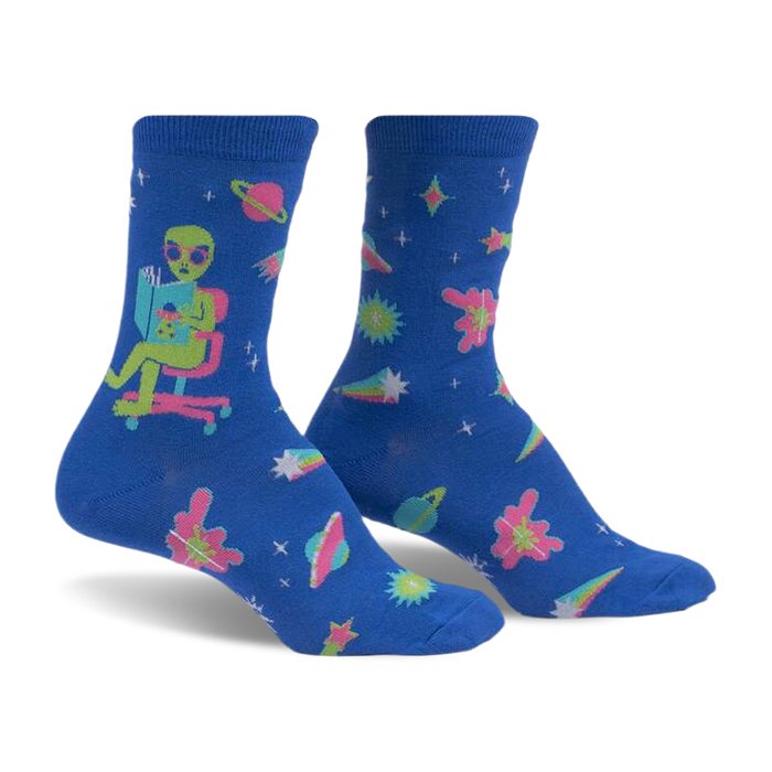 front view of a pair of blue socks with an alien reading a book in a chair, stars, planets and comets in pink, green, yellow and white.