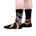 Lifestyle shot showing the 'Secret Powers' socks on a person's legs. The socks are predominantly black with yellow and red stripes.