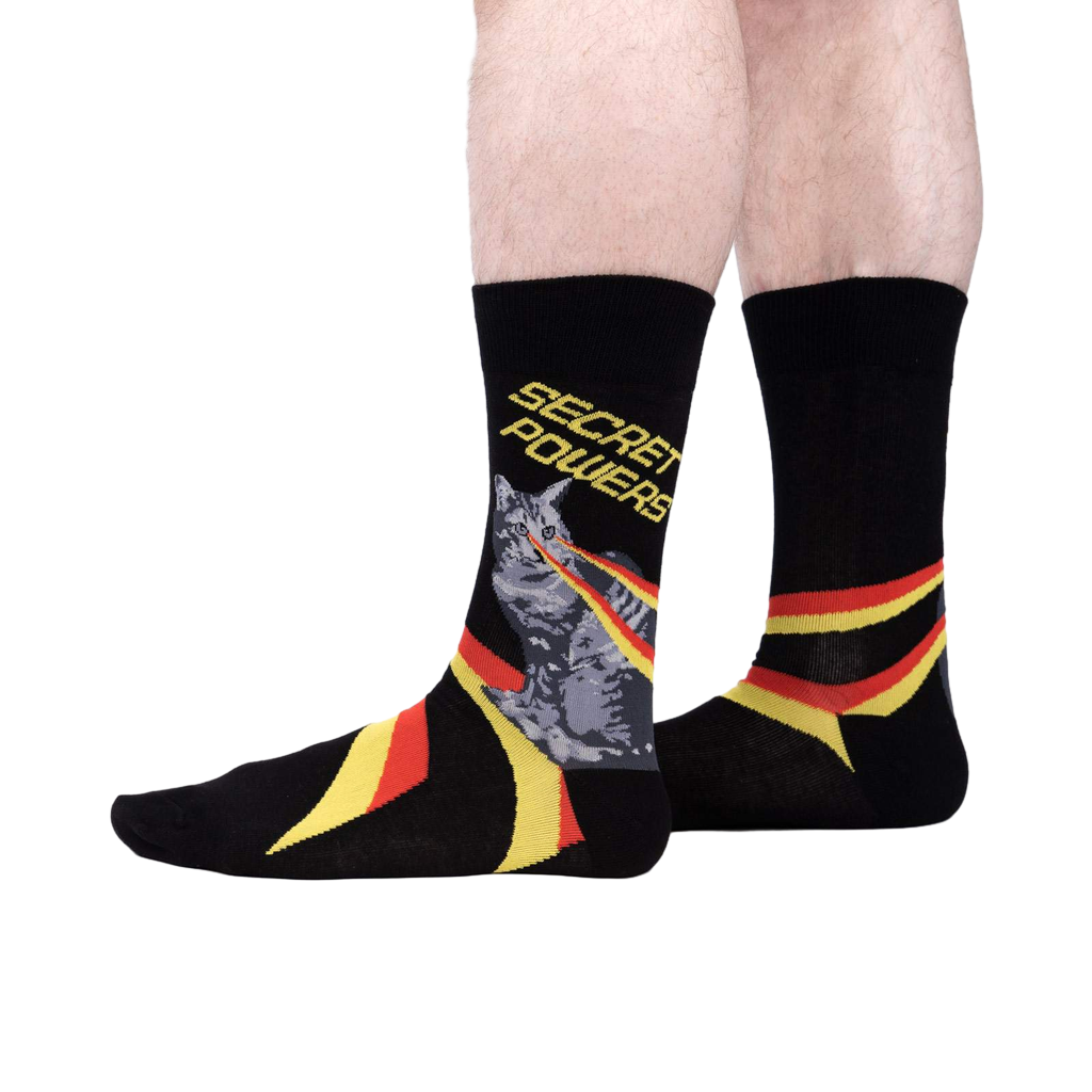 Lifestyle shot showing the 'Secret Powers' socks on a person's legs. The socks are predominantly black with yellow and red stripes.