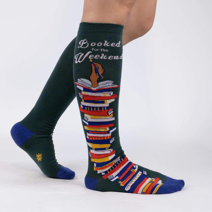 A pair of green knee-high socks with a pattern of books on them. The socks have the words 