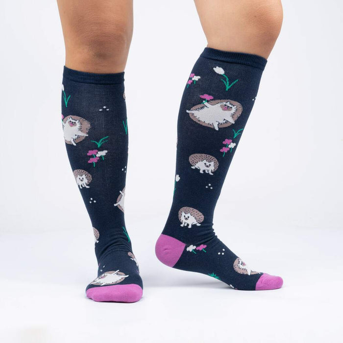 A pair of knee-high socks with a dark blue background and a pattern of hedgehogs and tulips. The socks have pink toes and heels.