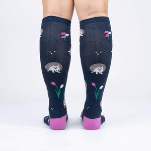 A pair of knee-high socks with a dark blue background and a pattern of hedgehogs and tulips. The socks have pink toes and heels.