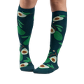 Lifestyle shot showing a person's legs wearing the teal avocado knee-high socks.