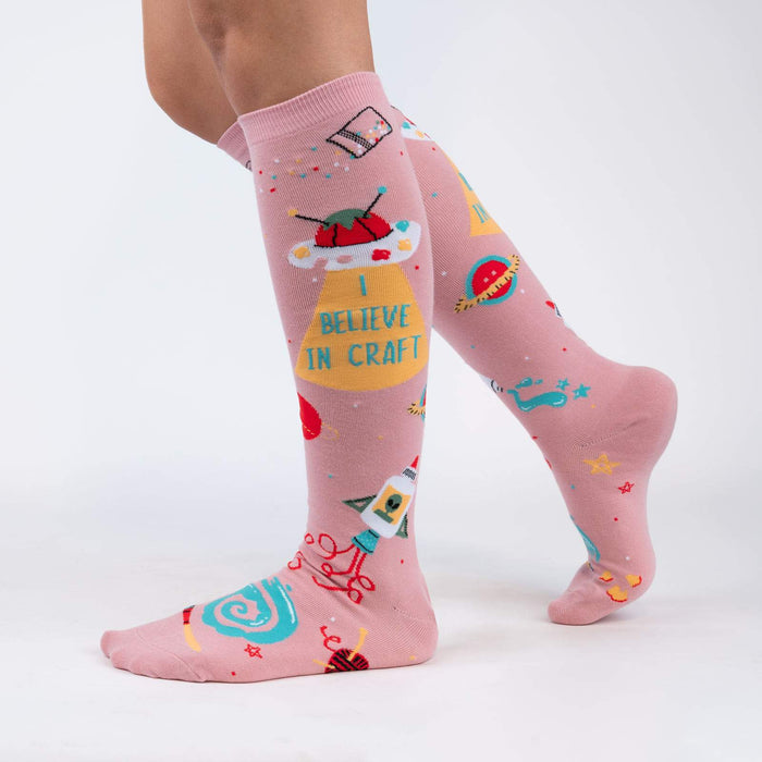 A pair of pink knee-high socks with a repeating pattern of measuring tapes, scissors, stars, and other sewing-related items.