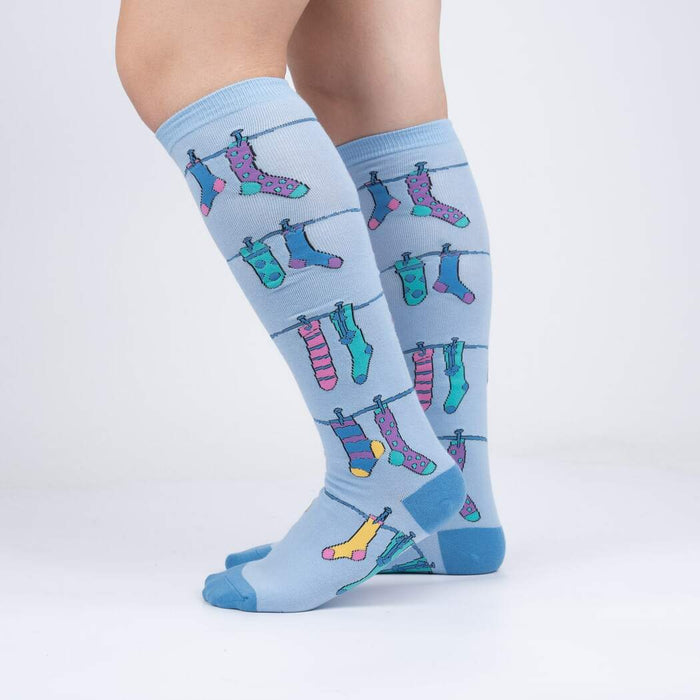 A pair of blue knee-high socks with a pattern of colorful socks hanging on a clothesline.