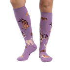 Lifestyle photo showcasing the lavender purple knee-high socks with dog illustrations on a person's legs.