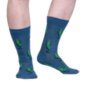 Lifestyle shot of model wearing a pair of blue crew socks with a fun pickle pattern.