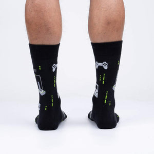A pair of black socks with a pattern of 8-bit video game controllers and systems. The socks are described as glowing in the dark.