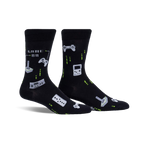 Pair of black crew socks with retro gaming controllers, joysticks, and pixelated designs in light green.  'Game On' text is also visible.