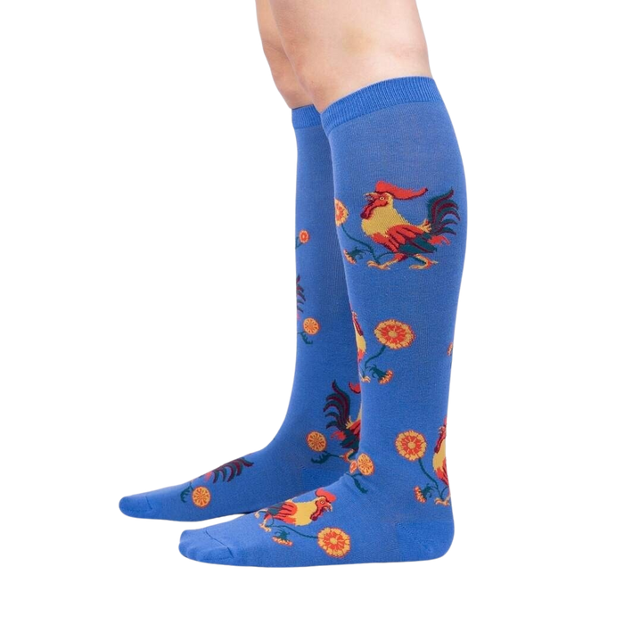A pair of blue knee-high socks with a pattern of red and yellow roosters and orange flowers.