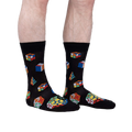 Lifestyle shot showing a person's legs wearing the Puzzle Box socks. The socks are black with colorful Rubik's Cube and geometric designs.