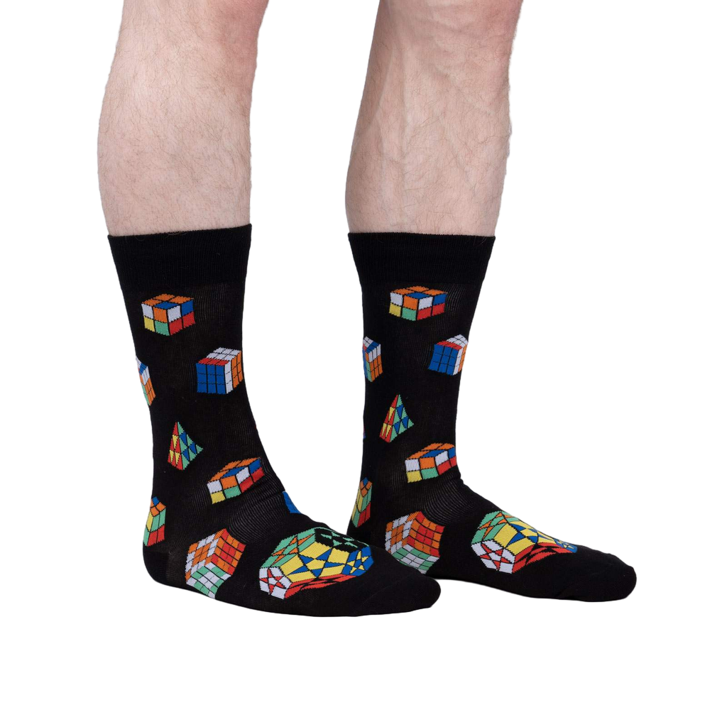 Lifestyle shot showing a person's legs wearing the Puzzle Box socks. The socks are black with colorful Rubik's Cube and geometric designs.