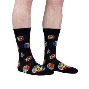 Lifestyle shot showing a person's legs wearing the Puzzle Box socks. The socks are black with colorful Rubik's Cube and geometric designs.
