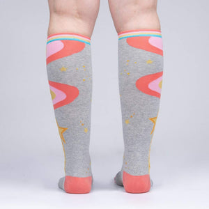 A pair of gray knee-high socks with a colorful pattern of pink, blue, and yellow waves and stars. The socks have pink toes and heels.