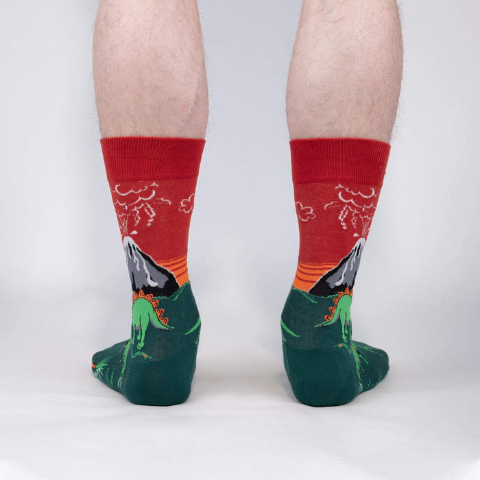 A pair of green and red socks with a dinosaur and volcano pattern.