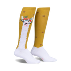 Pair of women's knee-high socks. Mustard yellow with white llama design wearing a flower crown. Small red and mustard flowers are scattered on the background.