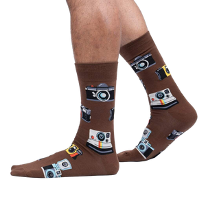 Lifestyle shot showing brown camera socks on a person's legs against a white background.