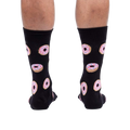 Rear view of model wearing black crew socks with pink donut pattern.