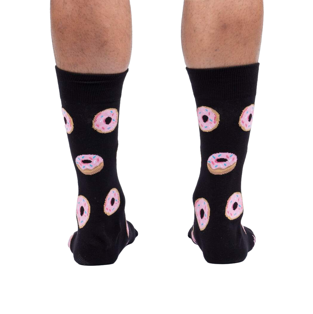 Rear view of model wearing black crew socks with pink donut pattern.