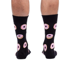 Rear view of model wearing black crew socks with pink donut pattern.