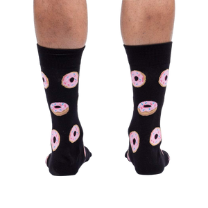 Rear view of model wearing black crew socks with pink donut pattern.