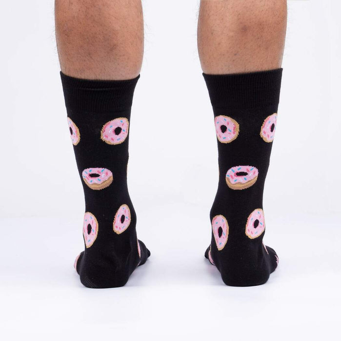 A pair of black socks with a pattern of pink donuts with blue, white, and yellow sprinkles.