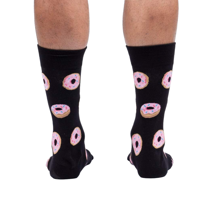Rear view of model wearing black crew socks with pink donut pattern.