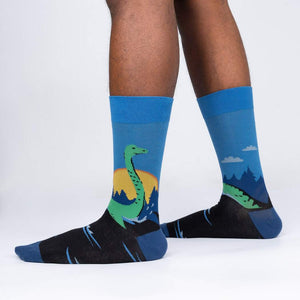 A pair of blue socks with a colorful pattern of mountains, trees, and a setting sun.