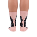 Back view of the socks on a person's legs. The socks are pale pink with black cats and hearts.