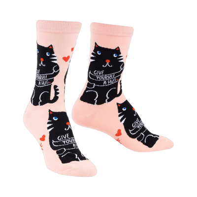 Crew socks in pale pink with a repeating pattern of black cats hugging themselves and the words 'Give Yourself A Hug'.