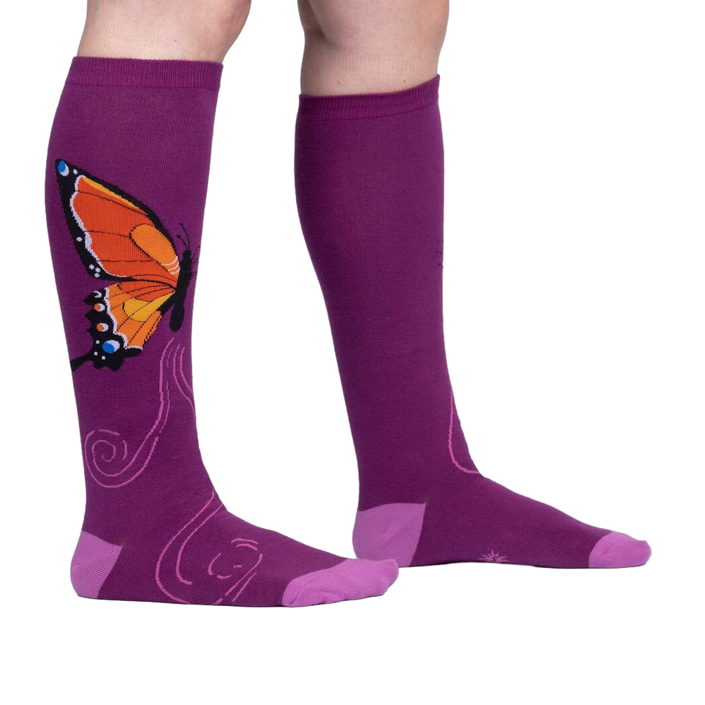 Flatlay: Two purple knee-high socks with an orange butterfly design are laid flat against a white background.