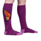 Flatlay: Two purple knee-high socks with an orange butterfly design are laid flat against a white background.