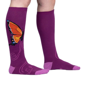 Flatlay: Two purple knee-high socks with an orange butterfly design are laid flat against a white background.