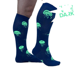 Close-up showing the 'Nice to Sea You' socks glowing in the dark, emphasizing the neon green jellyfish against the blue background.