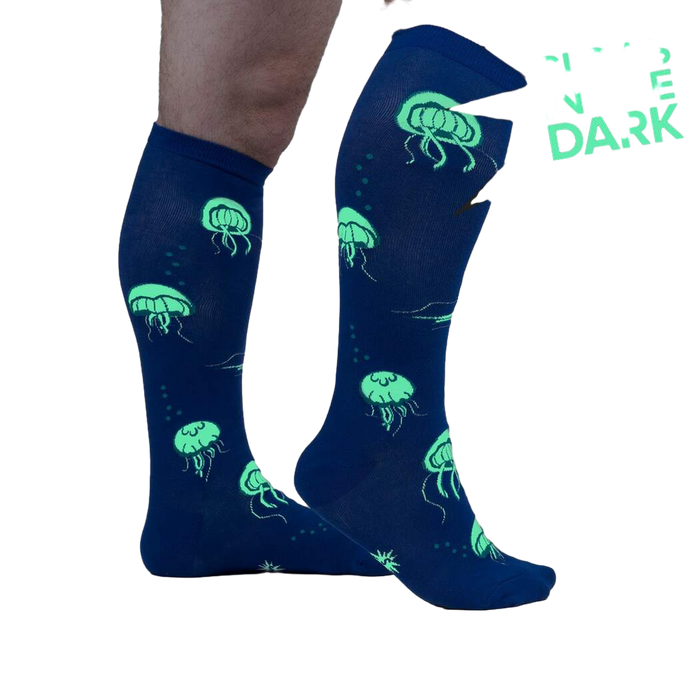 Close-up showing the 'Nice to Sea You' socks glowing in the dark, emphasizing the neon green jellyfish against the blue background.