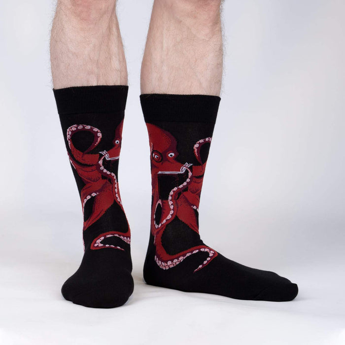 A pair of black socks with a red octopus design. The octopus is wearing glasses and holding a book.