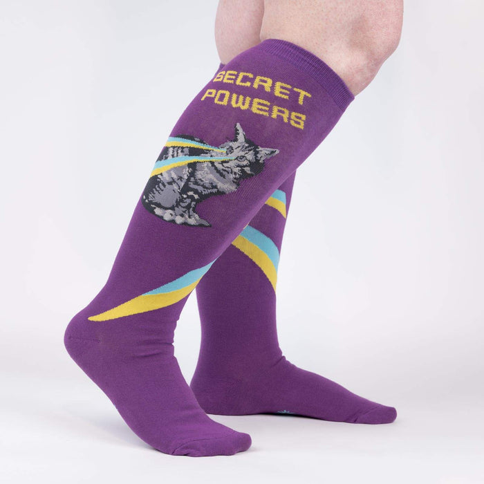 A pair of purple knee-high socks with a design of a narwhal swimming with a yellow and blue trail behind it. The word 