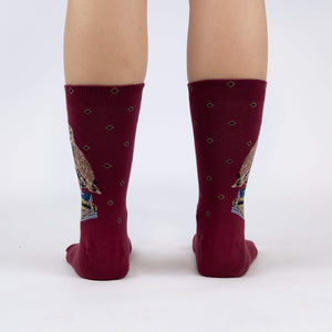 A pair of maroon socks with a pattern of blue and yellow diamonds. The socks have an image of an owl wearing a graduation cap and holding a book on each foot.
