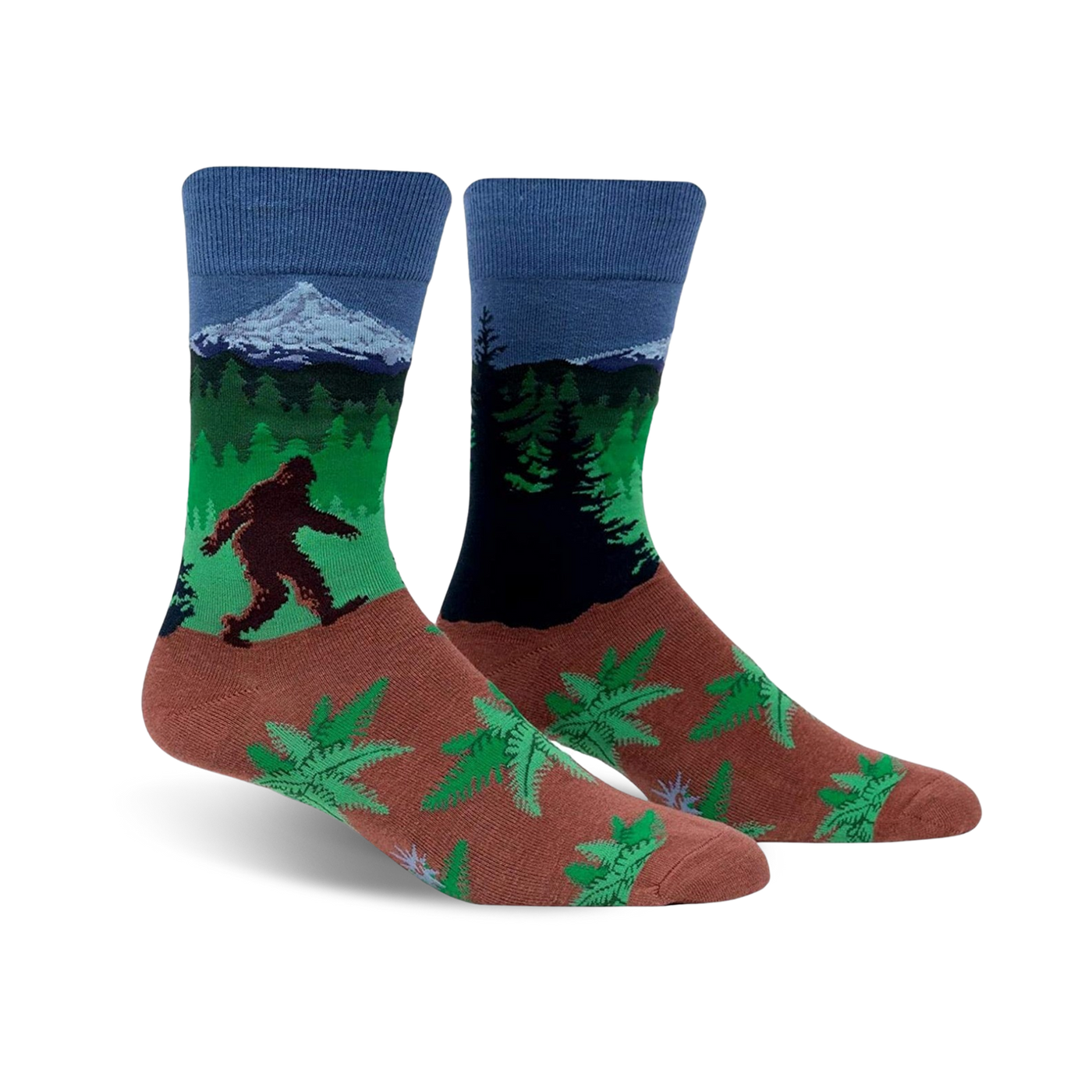 A pair of crew socks showcasing Bigfoot trekking through a forest landscape with a mountain in the background. The socks are predominantly blue, green, and brown, with a fern pattern at the bottom.